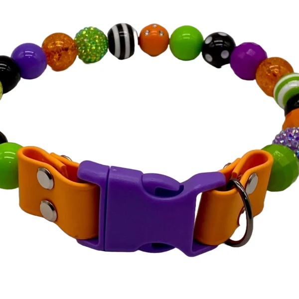 The Lime-Orange-Purple Beaded Dog Collar is colorful, with green, orange, purple, and black beads showcasing various textures and patterns. It features an orange and purple buckle along with a metal ring for leash attachment.