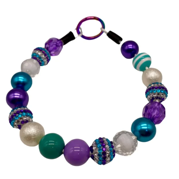 A vibrant dog collar featuring an array of bead sizes and textures in purple, teal, white, and metallic hues. Some beads are adorned with rhinestones, all linked by a metal ring at the top.