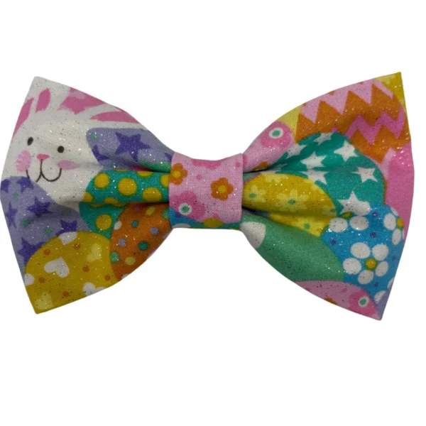 The Hoppy Easter Sparkle Pet Bowtie features a whimsical design with a smiling white rabbit, stars, polka dots, and zigzags in pink, yellow, green, and blue. Perfect for Easter celebrations with its subtle sparkle accent.