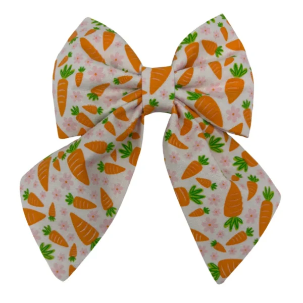 The Hoppy Harvest Sailor Bowtie showcases a playful, vibrant pattern of orange carrots and green leaves on a crisp white background, featuring two loops and tails.